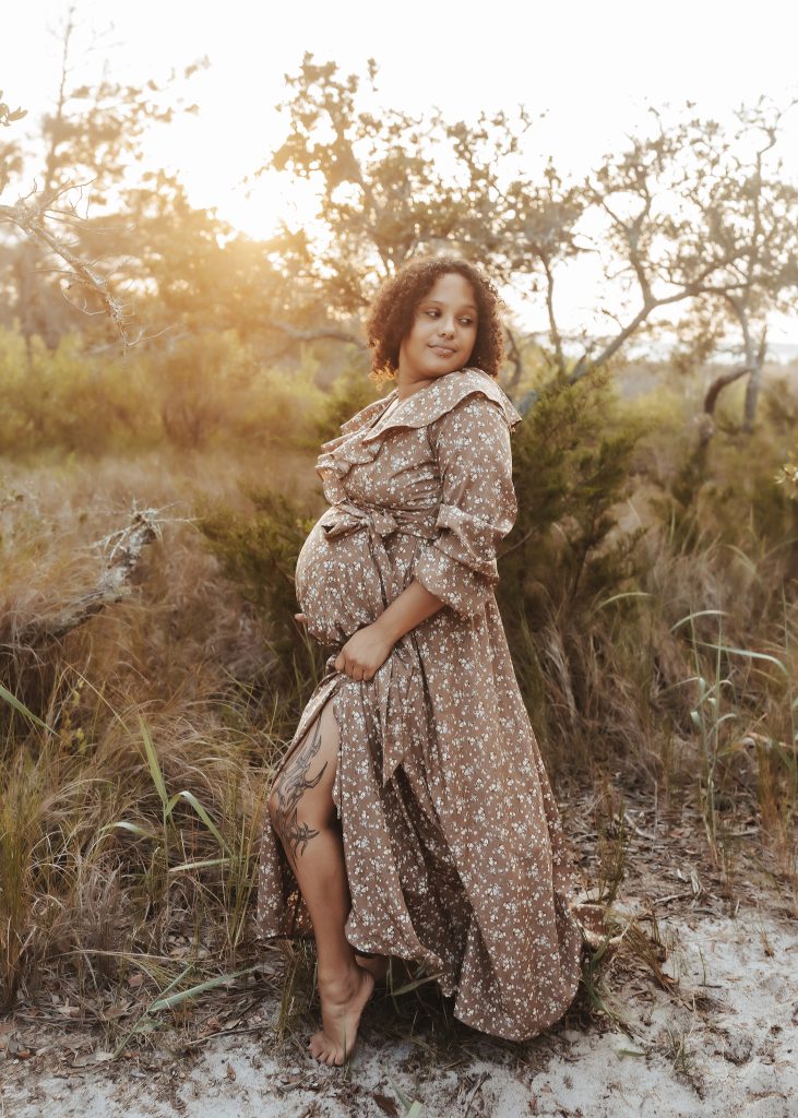 pregnant mom in brown floral dress holding her belly in a field 