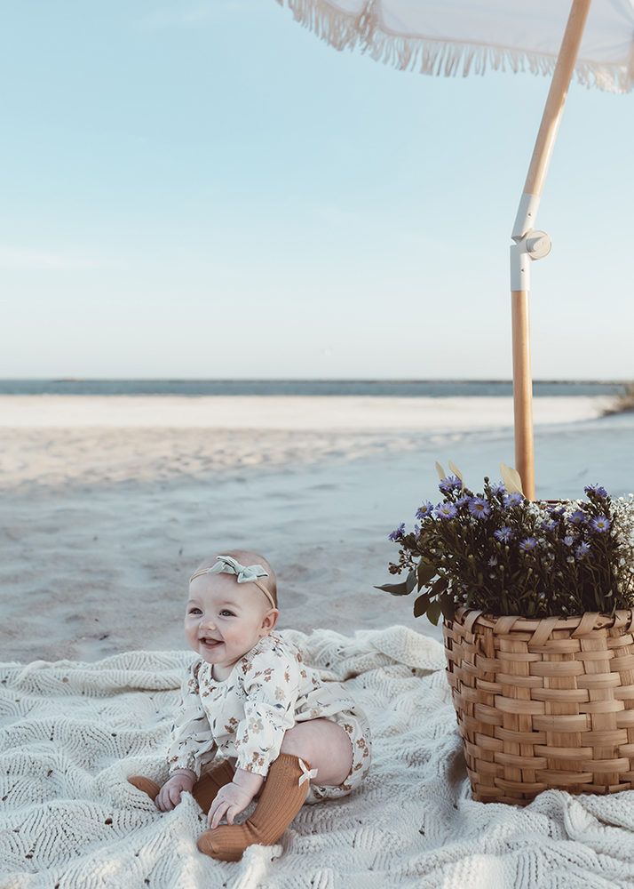 6 month old baby on the beach with flowers smiling