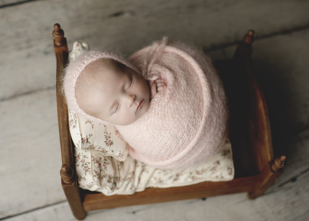 swaddle newborn on a small wooden bed